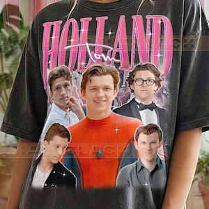 May include: Dark gray t-shirt featuring multiple images of Tom Holland, with the name "HOLLAND" in pink, and the word "Tom" in white script. The shirt has the text "PEPPER COMFORT COLORS" at the bottom.
