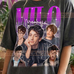 May include: A charcoal grey t-shirt featuring a graphic print of a person in various poses and outfits. The name MILO is printed in large purple letters at the top, with the word Manheim in white script below. The text PEPPER COMFORT COLORS is at the bottom.