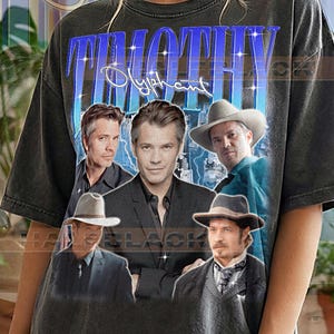 May include: Dark grey t-shirt with a graphic of Timothy Olyphant and the name "Timothy Olyphant" in blue. The shirt has a vintage appearance with multiple images of the actor. The text "Pepper Comfort Colors" is printed at the bottom.