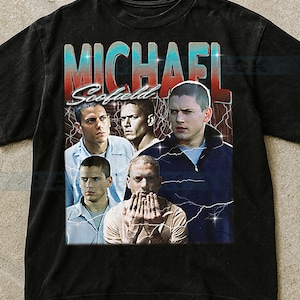 Op de afbeelding: Zwart t-shirt met een afbeelding van Michael Scofield uit de tv-serie Prison Break. Het ontwerp bevat meerdere afbeeldingen van het personage met de naam "MICHAEL Scofield" in een retro-stijl met bliksemschichten.