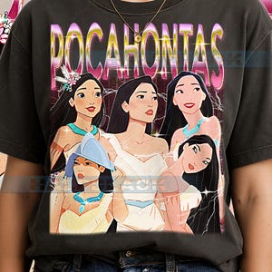 Può includere: T-shirt grigio scuro con una grafica di Pocahontas e altri personaggi del film d'animazione. La parola "POCAHONTAS" è stampata in un font rosa e giallo sopra i personaggi.