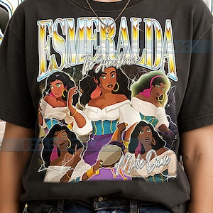 Op de afbeelding: Donkergrijs T-shirt met een afbeelding van Esmeralda uit De Klokkenluider van de Notre Dame. Het ontwerp bevat de tekst "Esmeralda" in een gele en witte letter, met meerdere illustraties van Esmeralda.