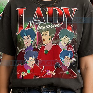 May include: Dark gray t-shirt featuring a graphic of Lady Tremaine from Cinderella. The design includes the word "LADY" in red, with "Tremaine" underneath. The image shows Lady Tremaine in a red dress with a green jewel.