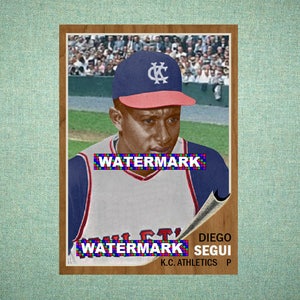 May include: A vintage baseball card featuring a player wearing a blue and red cap with a white KC logo and a white jersey with blue sleeves. The card includes the text DIEGO SEGUI and K.C. ATHLETICS P, with a stadium crowd visible in the background.