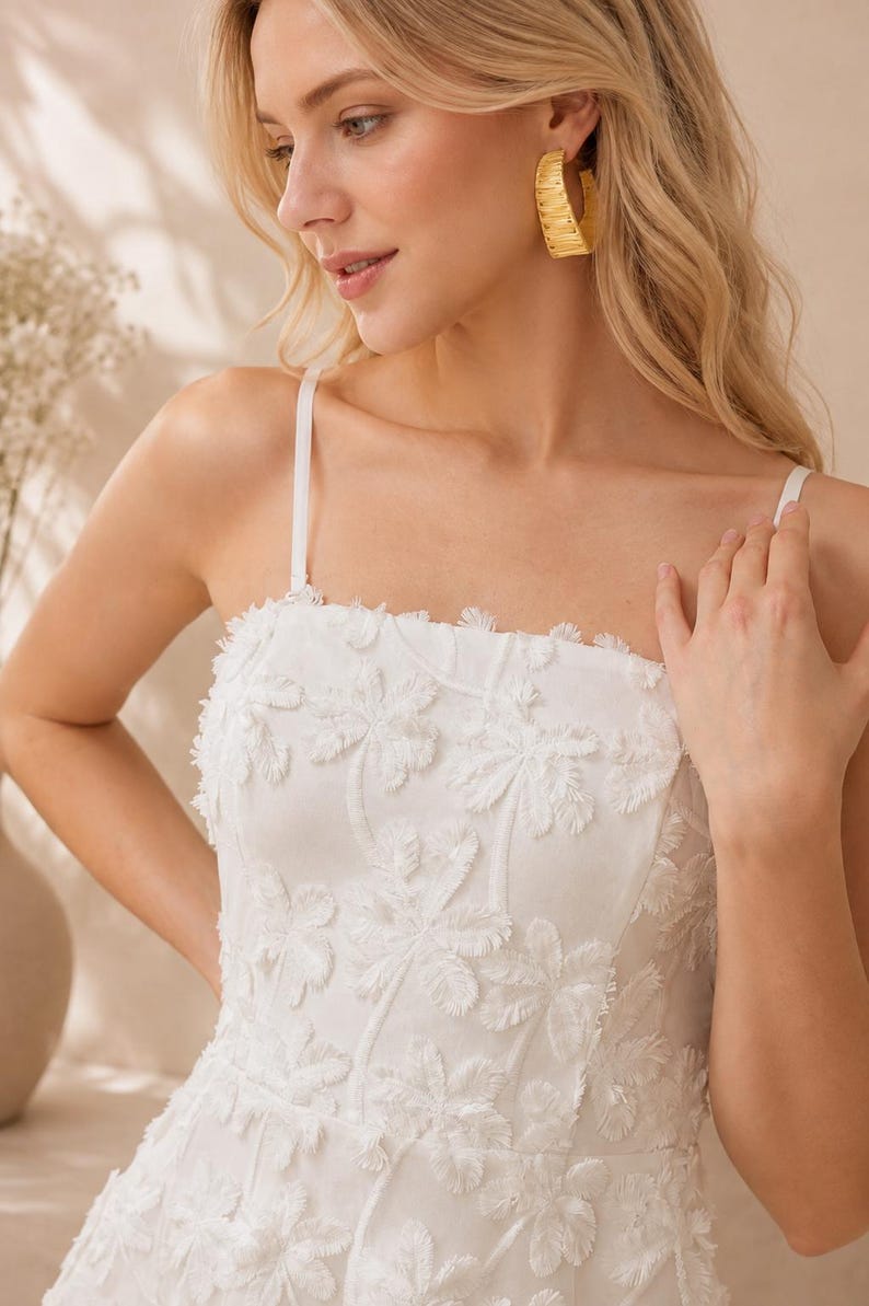 May include: A white sleeveless dress featuring a square neckline and thin spaghetti straps. The fabric is adorned with a textured, raised floral pattern with frayed edges throughout the bodice. The garment has a structured fit and clean lines.