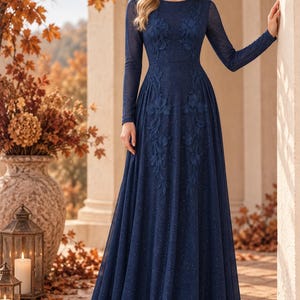 May include: A floor-length navy blue long-sleeve gown featuring a subtle glitter finish and intricate tonal floral embroidery extending from the bodice down to the waist. The dress has a round neckline and a flowing, full-length skirt silhouette.