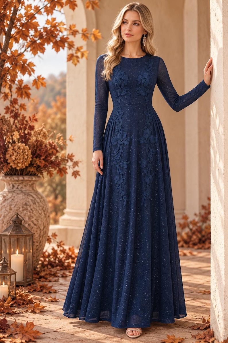 May include: A floor-length navy blue long-sleeve gown featuring a subtle glitter finish and intricate tonal floral embroidery extending from the bodice down to the waist. The dress has a round neckline and a flowing, full-length skirt silhouette.