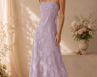 May include: A floor-length lavender dress featuring a square neckline, thin spaghetti straps, and an all-over textured floral appliqué pattern. The garment has a fitted bodice that transitions into a flowing skirt with a tie detail at the back.