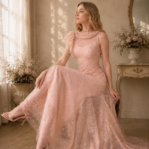 May include: A floor-length, pale pink sleeveless dress featuring a delicate lace overlay with a floral pattern, a high neckline with gathered fabric detail at the shoulder, and a fitted bodice that transitions into a flowing, sheer lace skirt.