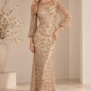 Puede incluir: Un vestido largo hasta el suelo de color champán con mangas largas y transparentes tipo obispo y cuello alto. El vestido está completamente adornado con intrincados patrones de lentejuelas y cuentas doradas dispuestos en un diseño geométrico de abanico.