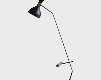 May include: A mid-century modern floor lamp with a black, double-cone shade and a brass-toned arm. The lamp features a small, cylindrical handle and a spherical base. The shade has small perforations for light diffusion.