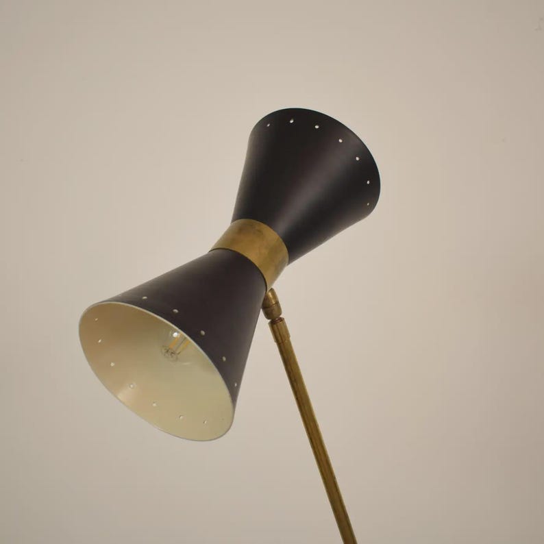 May include: A mid-century modern black and brass floor lamp. The lamp features two conical shades with a brass band and a brass stem. The interior of the shades is white. The lamp is a stylish addition to any room.