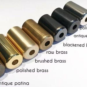May include: An assortment of cylindrical metal objects in various finishes, including polished chrome, antique black, and polished brass. The objects have a hole through the center and are arranged diagonally. Text labels identify each finish.