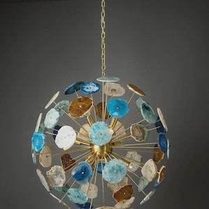 Pode incluir: Um lustre esférico decorativo, suspenso por uma corrente dourada. Apresenta uma estrutura dourada e é adornado com fatias de ágata polidas em vários tons de azul, castanho e branco. O design é moderno e atraente.