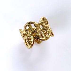 Può includere: Un anello color oro con un design a catena. L'anello è realizzato in un metallo lucido e riflettente e presenta una serie di maglie interconnesse. L'anello è un pezzo forte, adatto per aggiungere un tocco di eleganza a qualsiasi outfit.