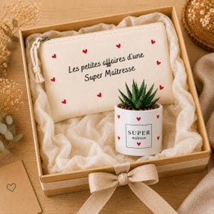 Könnte beinhalten: Eine Geschenkbox mit einer cremefarbenen Reißverschlusstasche mit roten Herzakzenten und dem Text "Les petites affaires d'une Super Maîtresse". Ein kleiner weißer Topf mit einer Sukkulente und roten Herzen befindet sich ebenfalls darin. Die Box ist mit einer beigen Schleife gebunden.
