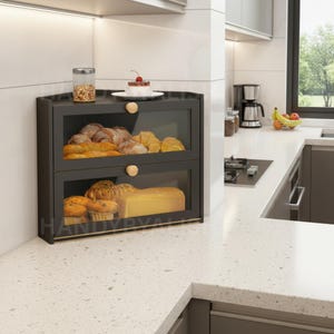 May include: A black, two-tiered bread box with glass doors and wooden knobs. The top shelf holds various baked goods, including croissants and bread. The bottom shelf displays muffins and a loaf of bread. A jar of granola and a cake are on top.