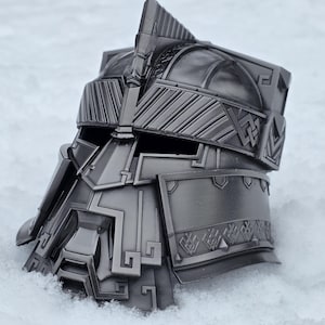 Peut inclure: Un casque gris métallique détaillé avec des motifs géométriques complexes et des formes angulaires. Le casque, probablement une pièce décorative, est posé sur un fond enneigé, soulignant sa surface texturée et son savoir-faire. Le design suggère un thème fantastique ou historique.