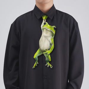 Könnte beinhalten: Schwarzes Button-Down-Hemd mit einem großen, realistischen Frosch-Design. Der grüne und weiße Frosch scheint das Hemd als Krawatte zu tragen. Das Hemd hat lange Ärmel.