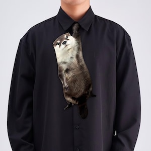 以下が含まれることがあります： 前面に登るカワウソのグラフィックが特徴の黒いボタンダウンシャツ。カワウソは茶色、白、黒の毛皮をしています。シャツは長袖で、クラシックな襟が付いています。