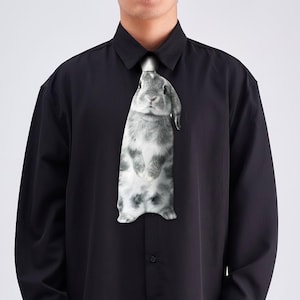 Könnte beinhalten: Schwarzes Hemd mit Knöpfen und einer ausgefallenen Krawatte mit einem grau-weißen Kaninchen-Design. Die Krawatte zeigt das Kaninchen in voller Länge und sorgt für einen einzigartigen Look. Das Hemd hat lange Ärmel.