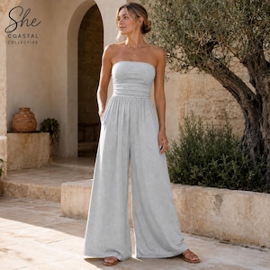 Könnte beinhalten: Ein hellgrauer trägerloser Jumpsuit mit einem eng anliegenden Oberteil mit dezenter horizontaler Raffung, einer definierten Taille und einer weit geschnittenen Hose mit Seitentaschen. Das Kleidungsstück besteht aus weichem, meliertem Stoff.