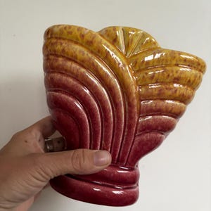 May include: A ceramic vase with a fan-shaped design. The vase has a colour gradient, changing from golden yellow at the top to deep red at the base. The vase has a glossy finish.