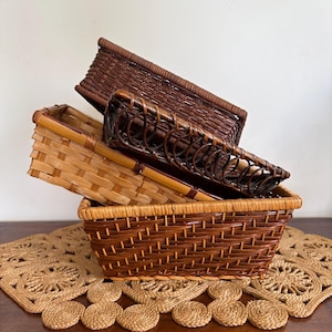 May include: Four rectangular woven baskets in shades of brown, stacked on top of each other. The baskets are made from natural materials, with light and dark brown hues. They rest on a decorative placemat with a circular pattern.