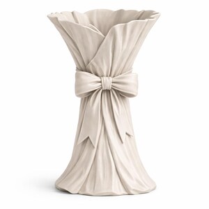 May include: Off-white ceramic vase with a draped fabric design. The vase is tied with a large bow at the center. The top of the vase has a ruffled edge, and the base flares out slightly.