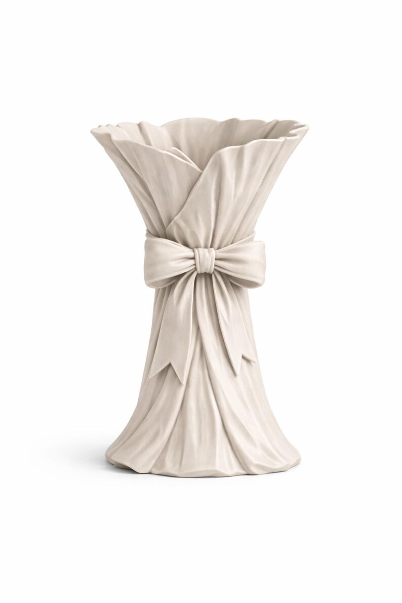 May include: Off-white ceramic vase with a draped fabric design. The vase is tied with a large bow at the center. The top of the vase has a ruffled edge, and the base flares out slightly.
