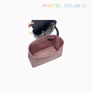 Puede incluir: Un organizador de bolso de color rosa polvoriento con múltiples compartimentos se muestra frente a un bolso negro acolchado. El organizador es rectangular y está diseñado para caber dentro de un bolso. El texto "PASTEL COLOR IN" está en la parte superior.