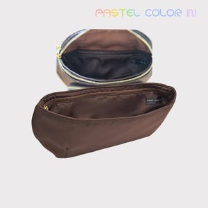 Könnte beinhalten: Eine offene schwarze Handtasche mit goldenem Reißverschluss und braunem Innenraum wird über einem braunen Organizer mit goldenem Reißverschluss gezeigt. Der Text "PASTEL COLOR IN" wird in Pastellfarben oben im Bild angezeigt.