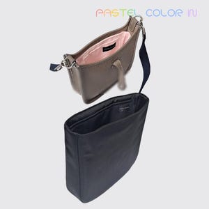 May include: A taupe leather crossbody bag with a pink interior and a black fabric insert. The bag has a long navy blue strap and silver-tone hardware. The text "PASTEL COLOR IN" is visible at the top.