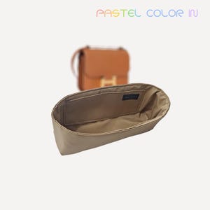 May include: A beige handbag organizer with a rectangular shape and multiple compartments. The organizer is made of a soft, fabric-like material. The text "PASTEL COLOR IN" is visible at the top of the image. A brown handbag is slightly out of focus in the background.