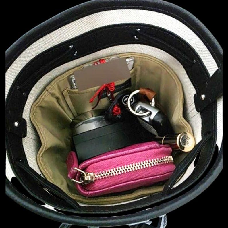 K&ouml;nnte beinhalten: Eine schwarz-wei&szlig; gestreifte Handtasche mit beigem Innenraum. Die Tasche enth&auml;lt ein pinkfarbenes Rei&szlig;verschlussetui, einen schwarzen Beh&auml;lter, Schl&uuml;ssel und einen Lippenstift. Das Innere der Tasche hat mehrere Taschen.