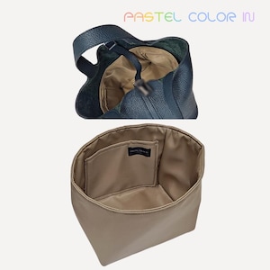 May include: A navy blue leather handbag with a top handle, showcasing the interior lining and a separate beige insert. The insert has a pocket with a black label. The text "PASTEL COLOR IN" is visible at the top.