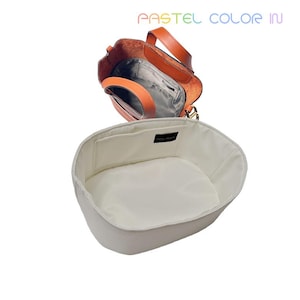 May include: An open orange leather handbag with a matching handle and a white interior organizer. The organizer has a rectangular pocket and a white interior. The text "PASTEL COLOR IN" is visible in the upper right corner.