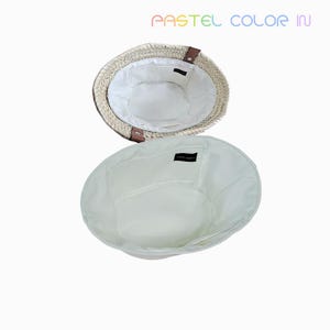 May include: Two open straw hats with white fabric lining. The hats have a natural woven texture with brown leather accents. The text "PASTEL COLOR IN" is displayed in rainbow colors at the top of the image.