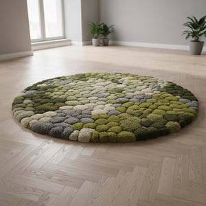 May include: A round rug with a textured surface, featuring a pattern of green, gray, and beige tufts. The rug is placed on a light-colored wooden floor, creating a natural and organic aesthetic. The rug's diameter is approximately 60 inches.