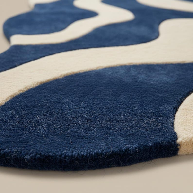 K&ouml;nnte beinhalten: Nahaufnahme eines blauen und cremefarbenen Teppichs mit Wellenmuster. Der Teppich hat eine weiche, strukturierte Oberfl&auml;che. Das Design zeigt flie&szlig;ende, organische Formen in einer kontrastierenden Farbpalette.