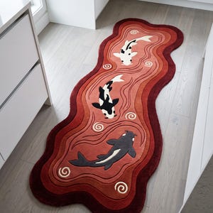 May include: An elongated, wavy-edged rug featuring a gradient of red and burgundy tones. The design depicts three koi fish in white, black, and dark gray, swimming amidst swirling water patterns that are carved into the textured surface of the rug.