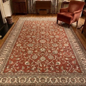 Hand knotted Persian style rug with rust base and floral vine pattern in traditional living room setting