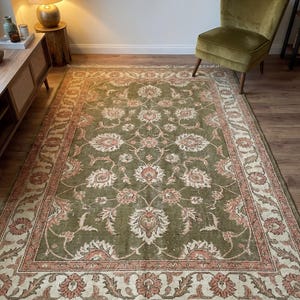 May include: A large, rectangular area rug with an intricate floral pattern in shades of olive green, cream, and peach. The rug has a detailed border and fringe along the edges, suitable for a living room or bedroom.