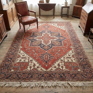 May include: A large, rectangular rug with a central geometric pattern in red, cream, and navy blue. The rug has a detailed border and fringing along the edges. It is placed on a wooden floor, adding warmth to the room.