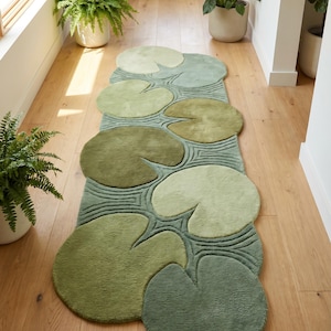 May include: A long, rectangular runner rug featuring a repeating pattern of overlapping lily pad shapes in various shades of green, including sage, olive, and lime, with carved linear details representing water ripples between the leaves.