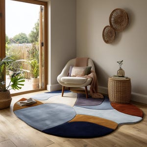 May include: A modern living room rug with an abstract design in shades of blue, tan, and rust. The rug is placed in front of a white armchair with wooden legs. A small wicker side table and decorative wall baskets complete the scene.