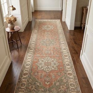 May include: A long rectangular runner rug featuring a faded terracotta orange and sage green floral medallion pattern with a cream border and fringed ends. The rug displays a symmetrical design with intricate botanical motifs throughout the centre.