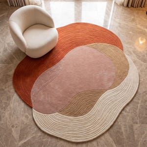 Könnte beinhalten: Abstrakter Teppich mit einem geschichteten Design in Rost-, Blush-Pink-, Beige- und Cremetönen. Der Teppich liegt auf einem Marmorboden, mit einem weißen Sessel in der oberen linken Ecke. Das Design ist organisch.