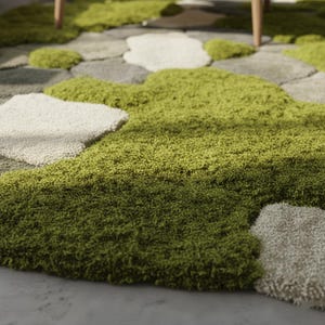 May include: A green and gray area rug with a unique design. The rug features a textured, moss-like appearance in shades of green, with stone-shaped accents in gray and off-white. The rug is designed to resemble a natural landscape.