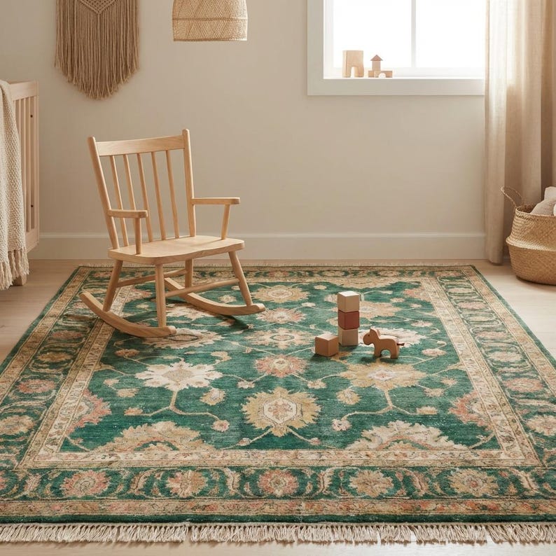 May include: A green and beige patterned area rug with a fringed edge. A light wood rocking chair sits on the rug. Wooden blocks and a toy horse are on the rug. The room has a neutral color palette.